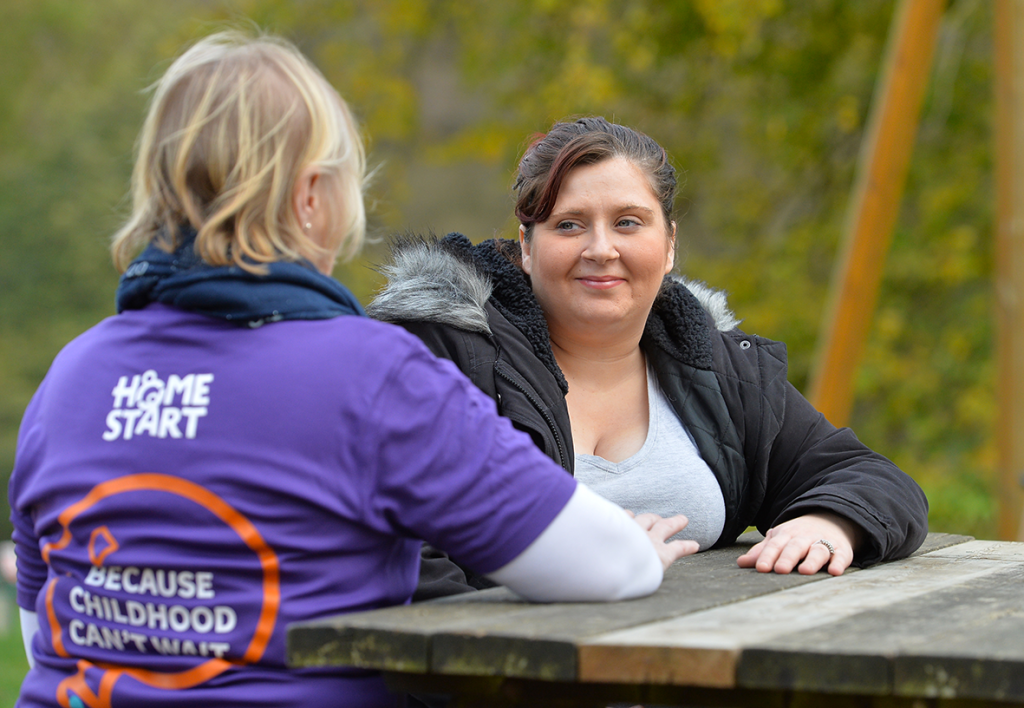 Two women chat at a picnic table, one is wearing a HomeStart t-shirt