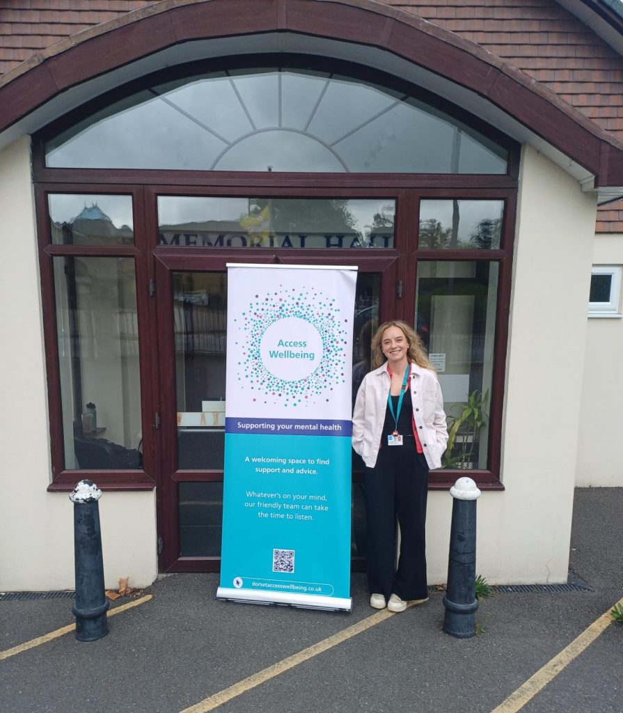 A wellbeing coordinator stands next to a banner outside the new Verwood drop-in space